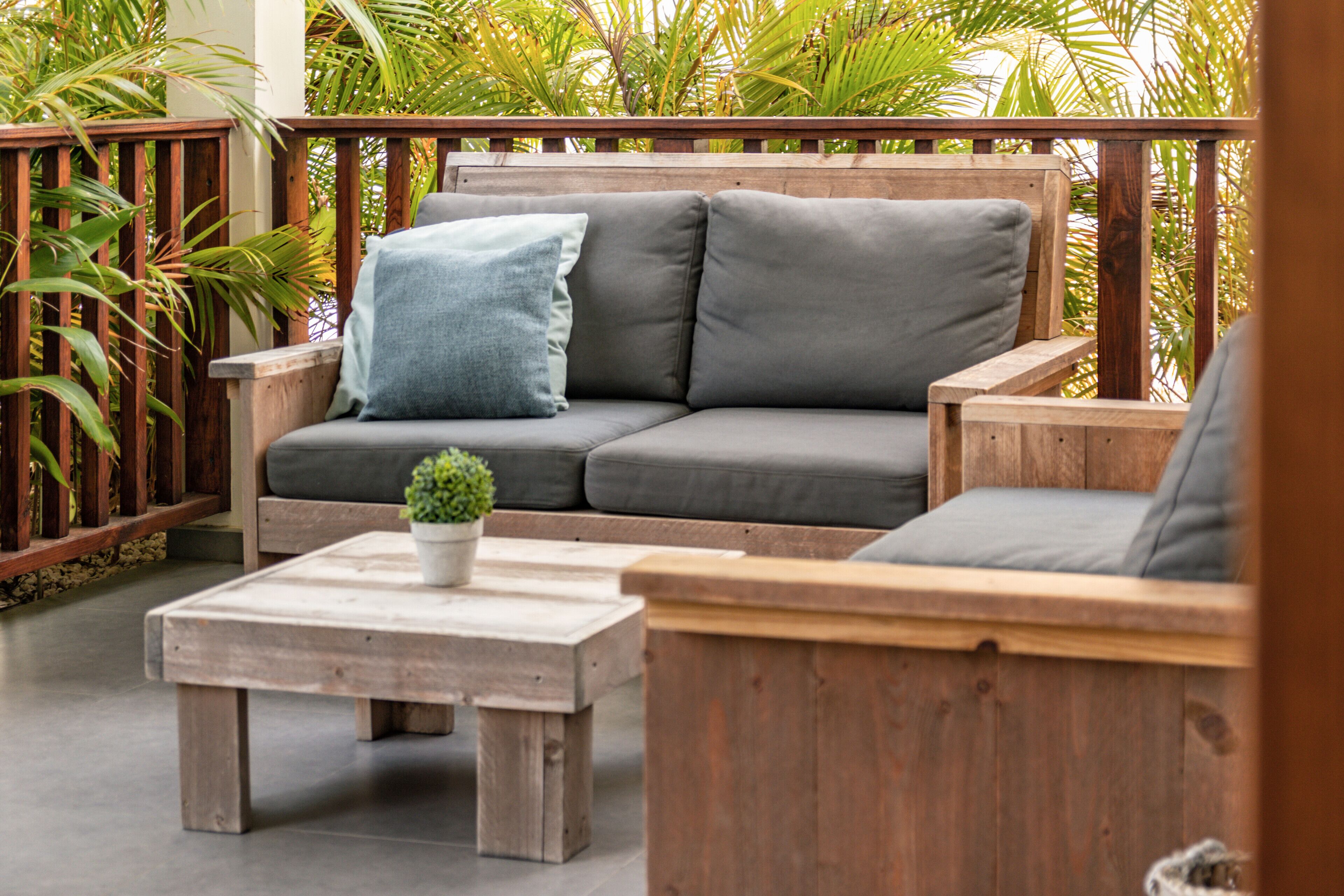 Een houten terras met een grijze bank, een kleine tafel met een plant en houten stoelen.
