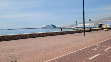 A waterfront promenade with a stone wall, a large cruise ship, and a blue building with a glass structure.