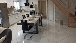 A modern kitchen with a dining area, featuring a long table, chairs, and a staircase leading to another level. - Country cottage near the Baie de Somme - Le Clos de R & R (Cambron)