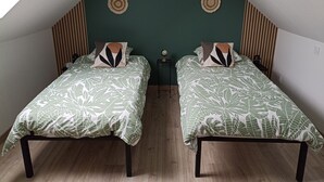 A room with two beds, each with a leaf-patterned bedspread, wooden headboards, and a dark green accent wall. - Country cottage near the Baie de Somme - Le Clos de R & R (Cambron)