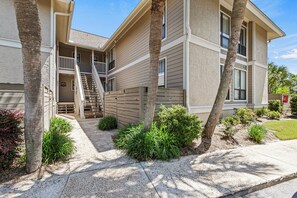 A two-story building with a balcony, a staircase, and a well-maintained garden with palm trees and shrubs.