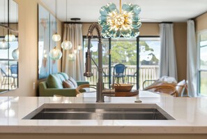A kitchen with a stainless steel sink, a modern faucet, and a decorative glass light fixture above the sink. - Palm Bay, Condo, Beach, Golf Cart, Pools (Miramar Beach)