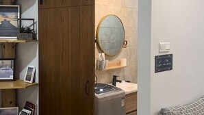 A room with a wooden wardrobe, a round mirror, a washing machine, and a bed with a striped blanket. - Buddy Station (Semporna)