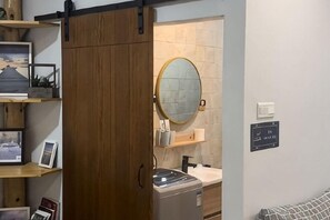 A room with a wooden wardrobe, a round mirror, a washing machine, and a bed with a striped blanket. - Buddy Station (Semporna)