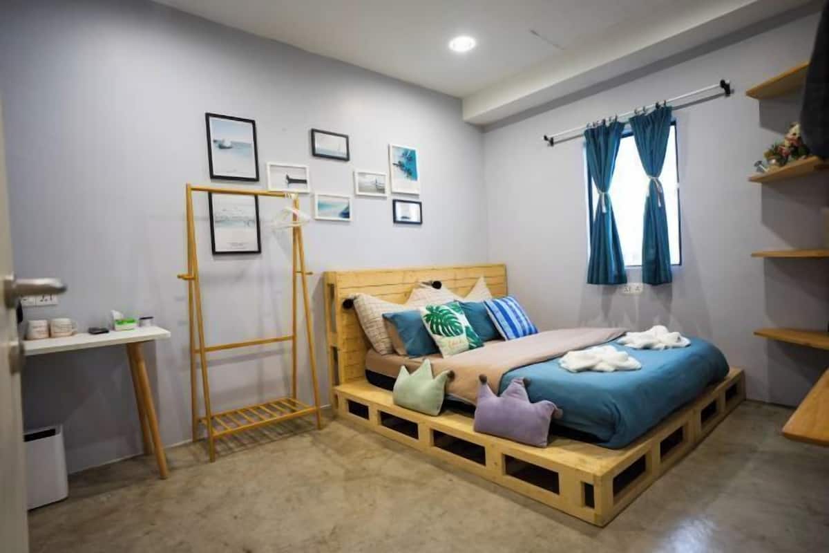 A bedroom with a bed, a desk, a ladder, and a window with curtains.