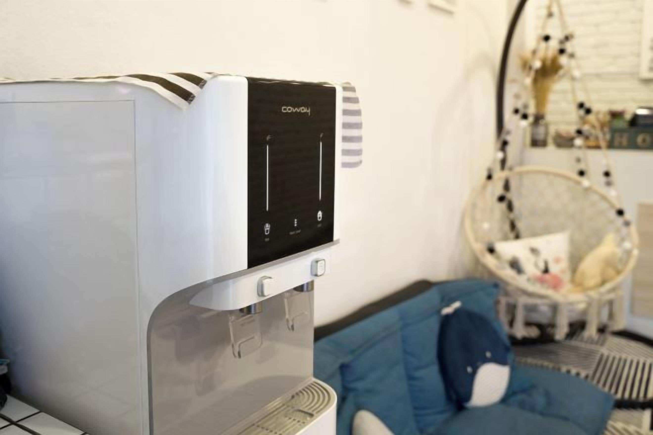 Een waterdispenser met een digitaal scherm, een blauwe bank en een hangstoel in een kamer.