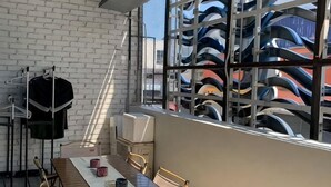 A room with a dining table, chairs, a window with a view of boats, a white brick wall, and a clothes rack. - Buddy Station (Semporna)
