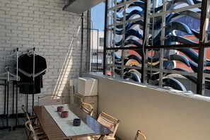 A room with a dining table, chairs, a window with a view of boats, a white brick wall, and a clothes rack. - Buddy Station (Semporna)