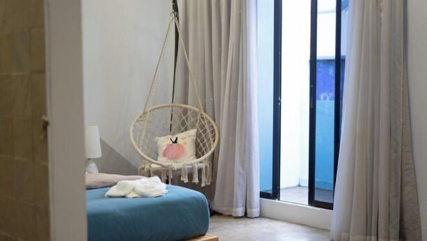 A bedroom with a bed, a hanging chair, a window with curtains, and a view outside. - Buddy Station (Semporna)
