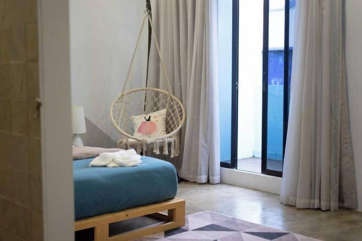 A bedroom with a bed, a hanging chair, a window with curtains, and a view outside.