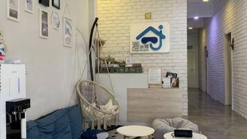 A reception area with a white brick wall, a reception desk, a hanging chair, a sofa, and a small round table.