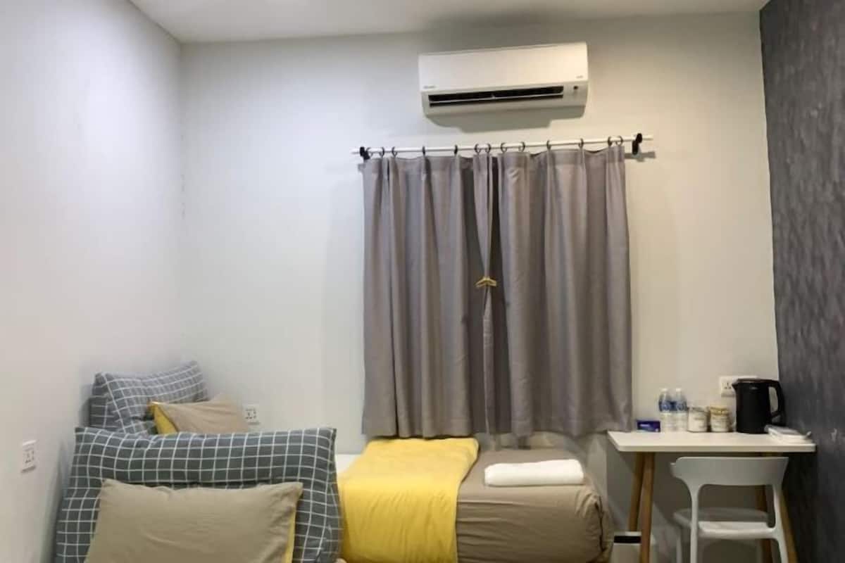 A small, neatly arranged room with a bed, a desk, and an air conditioning unit.