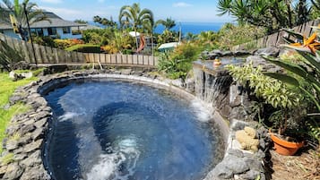 Une source thermale entourée d’une clôture en bois, de plantes tropicales et offrant une vue sur l’océan.