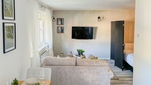 Una sala de estar moderna con un sofá, un televisor de pantalla plana montado en la pared y un rincón de comedor con una mesa para dos.