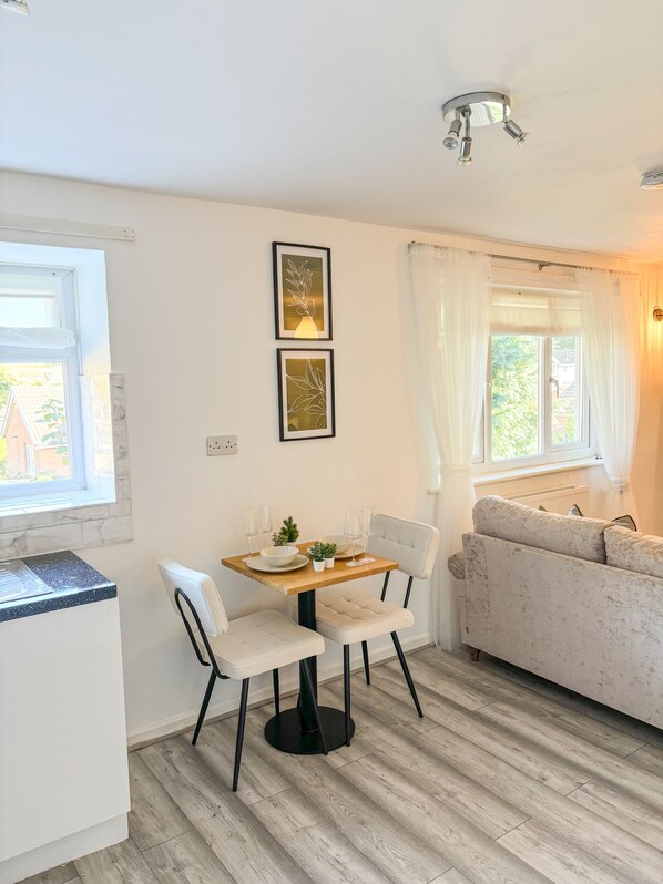 A modern living room with a dining area, featuring a wooden table, white chairs, a sofa, and a ceiling light fixture. - Manchester Luxury Studio Apartment (Manchester)