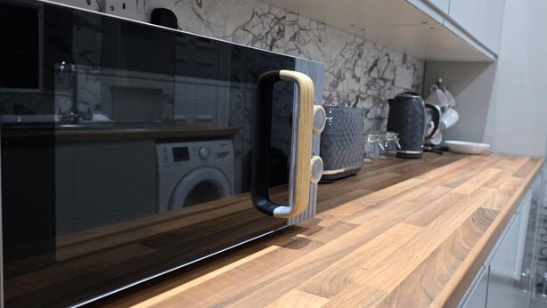 A kitchen with a modern design, featuring a wooden countertop, a microwave with a wooden handle, and a marble backsplash. - Cozy Newcastle Apartment With 2 Bedrooms (Newcastle-upon-Tyne)