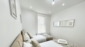 A hotel room with two beds, a window with blinds, a mirror, and a radiator. - Cozy Newcastle Apartment With 2 Bedrooms (Newcastle-upon-Tyne)