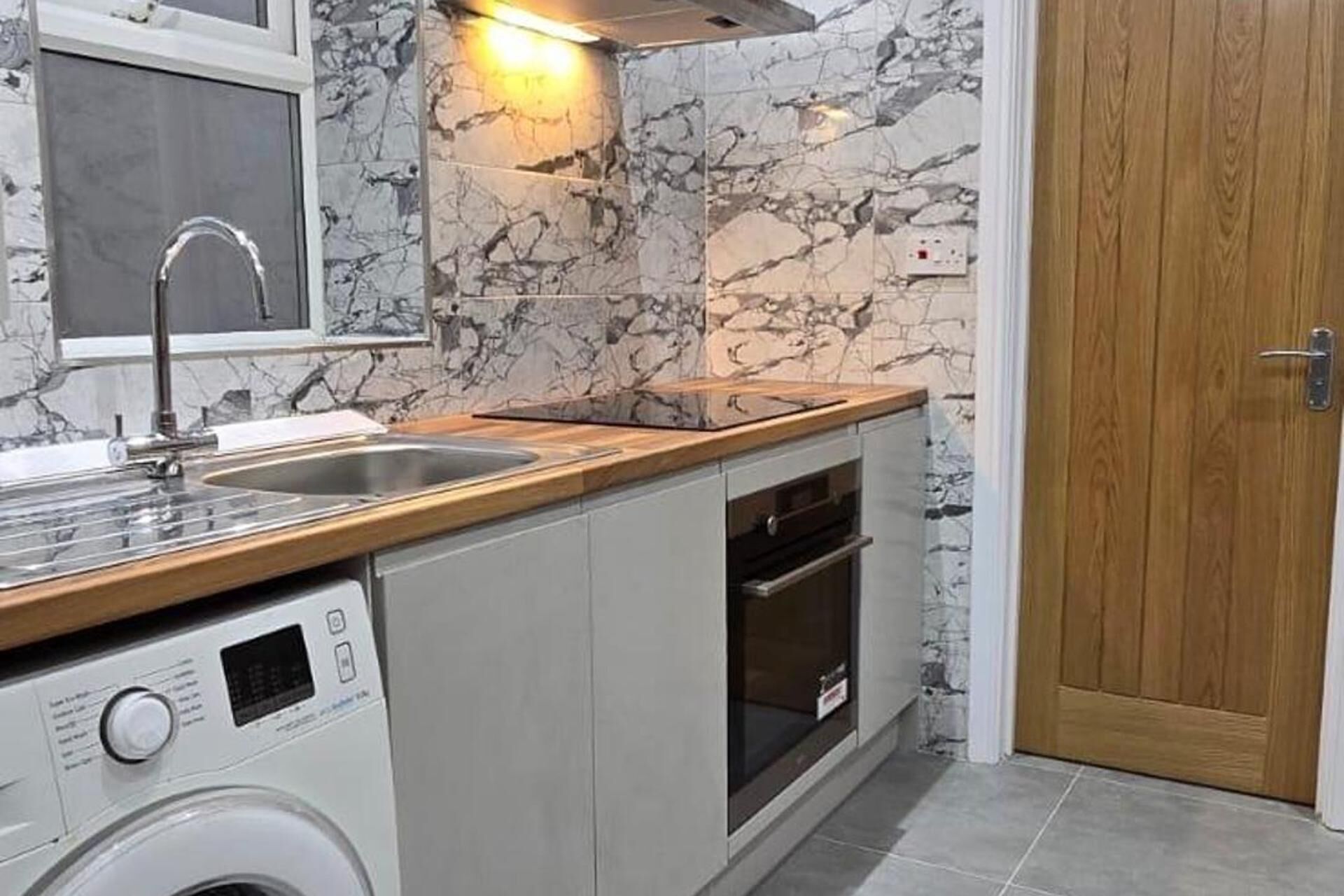 A compact kitchen with a washing machine, a sink, and a wooden countertop.