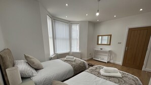 A modern bedroom with two beds, a bedside table with a lamp, a dresser, and a mirror on the wall. - Cozy Newcastle Apartment With 2 Bedrooms (Newcastle-upon-Tyne)