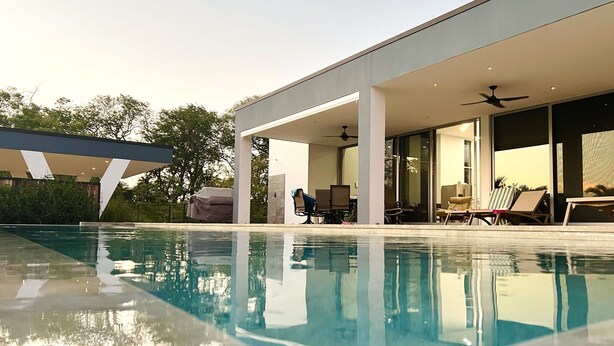 A modern house with a swimming pool, outdoor seating, and a covered patio area.