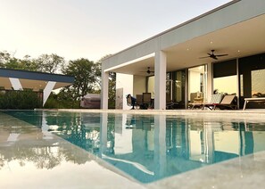 Una casa moderna con piscina, mobiliario de exterior y un patio cubierto.
