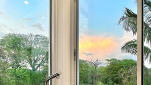 A kitchen with two stainless steel sinks and a window overlooking a forested area with a sunset view.