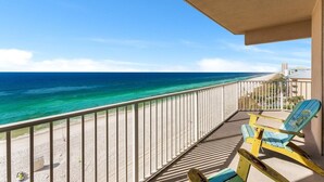 Ein Balkon mit Blick auf das Meer und den Strand, ein Stuhl und ein kleiner Tisch.