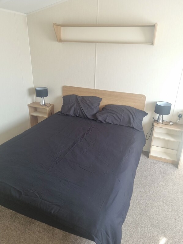Una cama con cabecera de madera, dos mesitas de noche con lámparas y un estante sobre la cama.