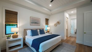 A modern bedroom with a large bed, bedside tables, a ceiling fan, and a view of the bathroom. - Coastal Luxury Home with Pool, Spa & Gourmet Kitchen (Naples)