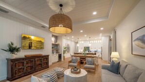 A spacious living room with a large sofa, a coffee table, and a dining area with chairs and a table. - Coastal Luxury Home with Pool, Spa & Gourmet Kitchen (Naples)
