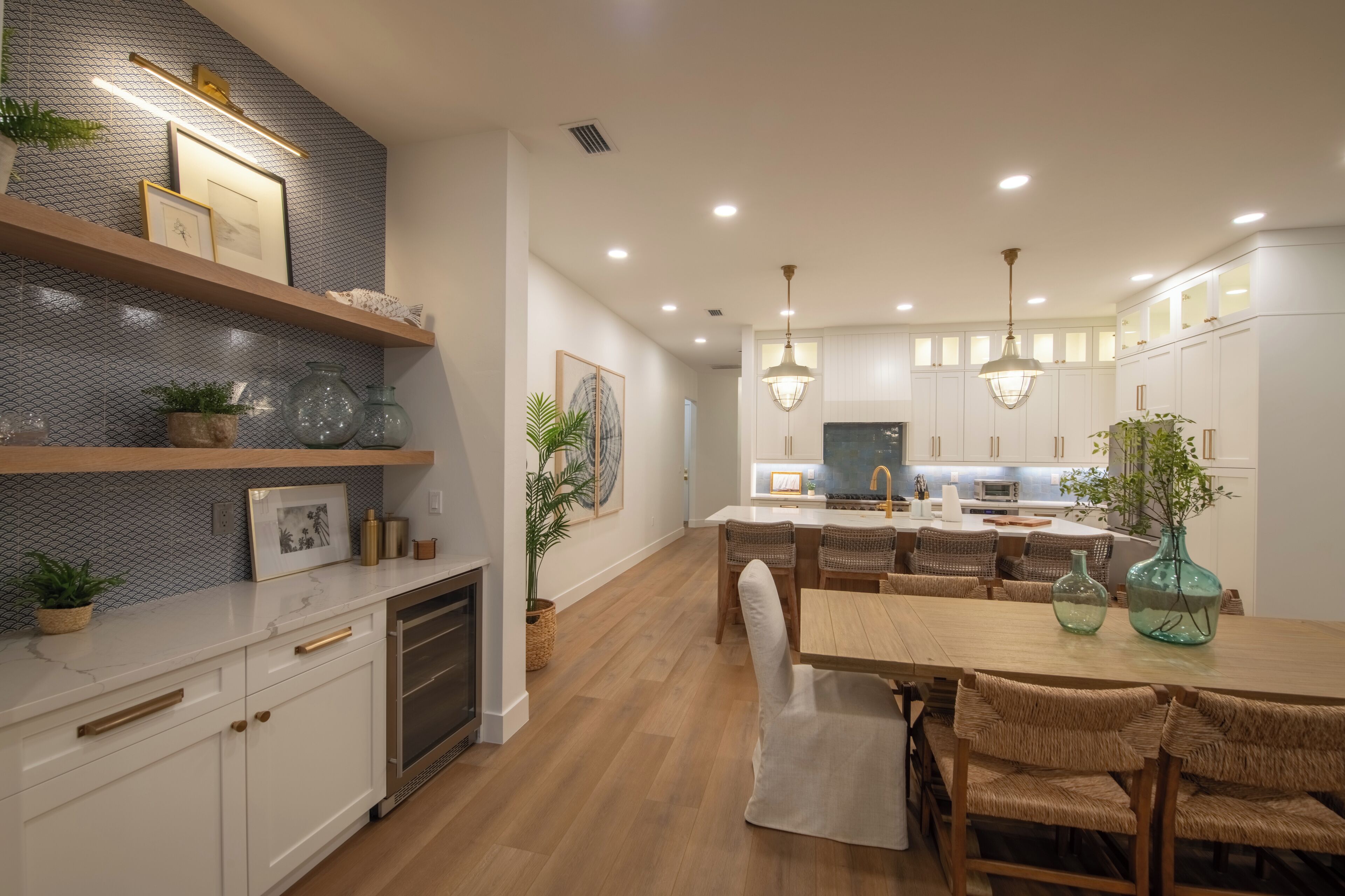 A modern kitchen with white cabinetry, wooden flooring, and a dining area with wicker chairs.