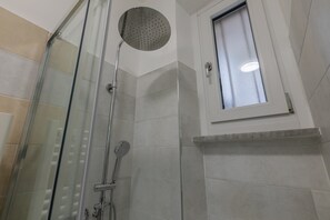 Douchegedeelte met een glazen deur, een handdouche en een raam boven de douche.