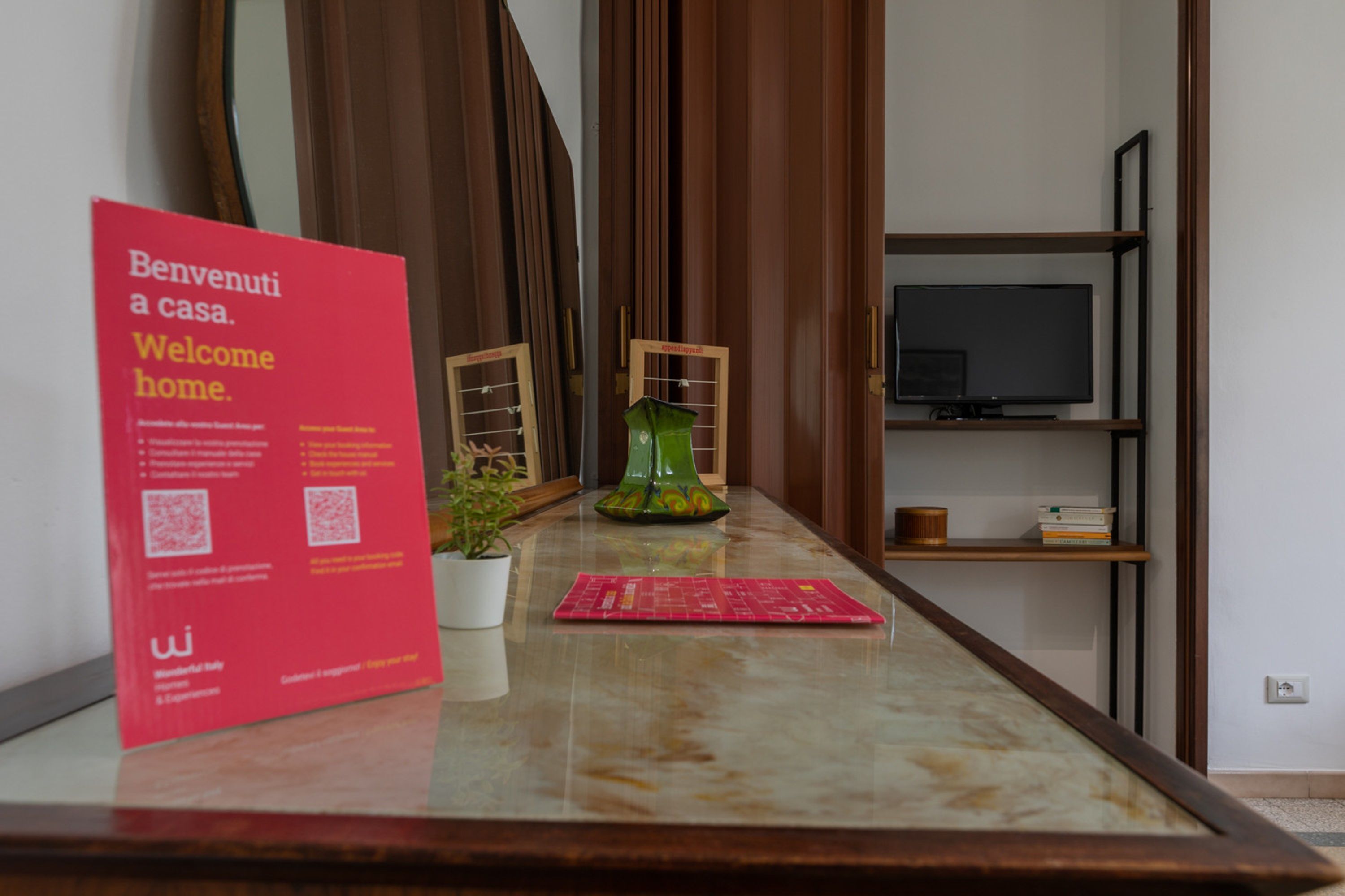 A reception desk with a red welcome sign, a potted plant, a green vase, and a television on a shelf.
