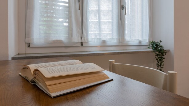 An open book on a wooden table by a window with white curtains. - A Casa di Ines by Wonderful Italy (Turin)