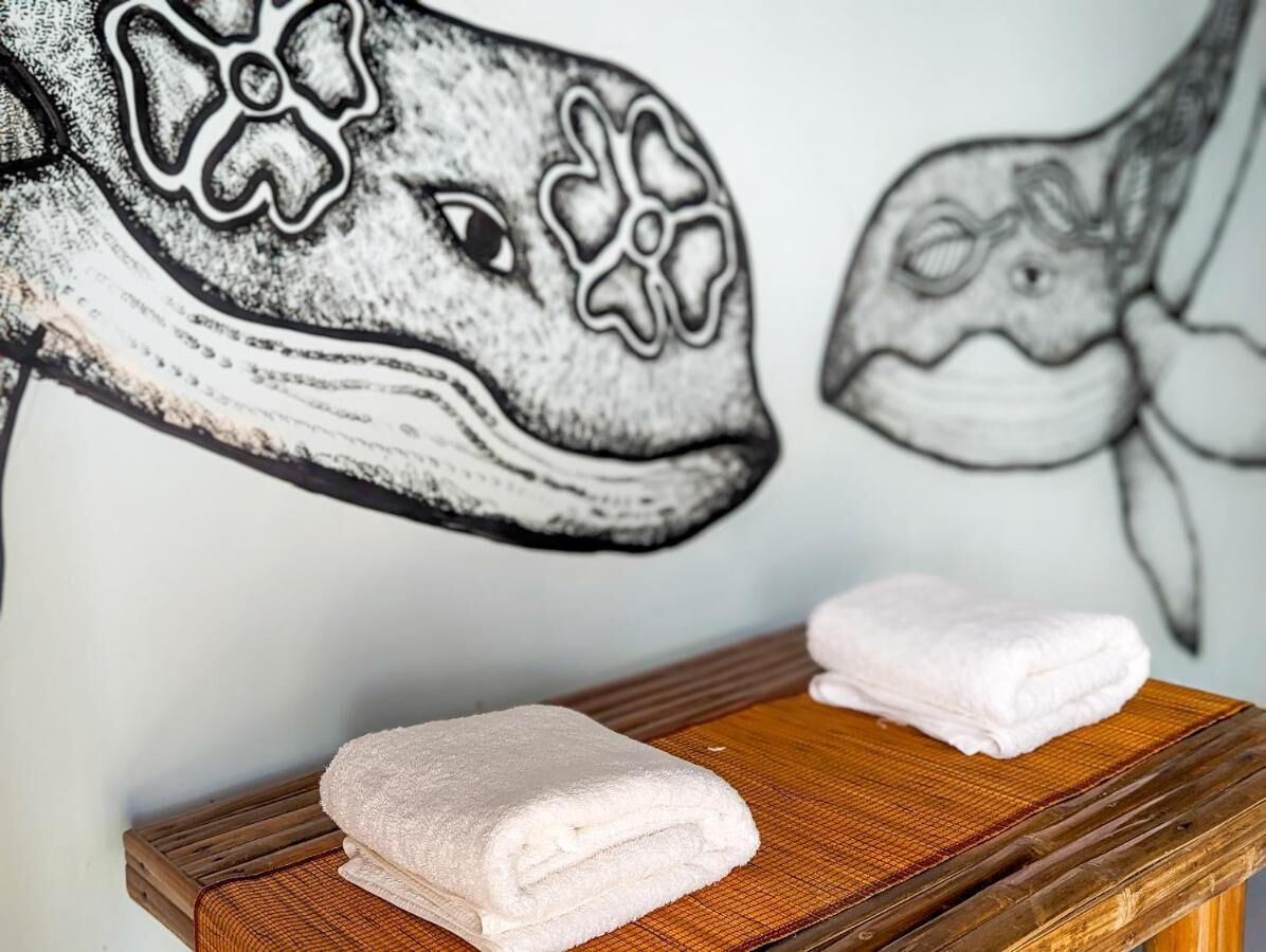 Ein Badezimmer mit einer Holzbank, zwei gefalteten Handtüchern und einem Wandbild von einem Fisch.