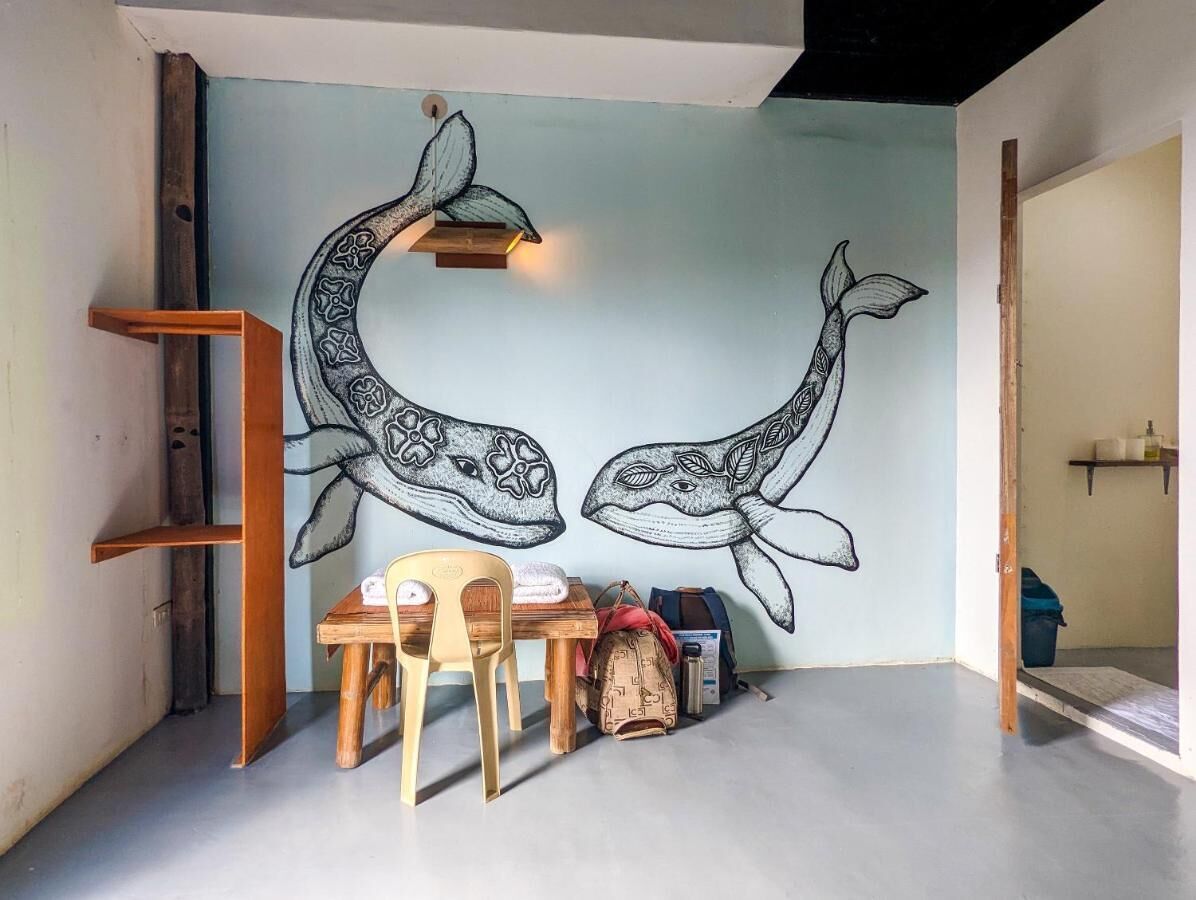 A room with a mural of two whales, a wooden table with chairs, and a ladder against the wall.
