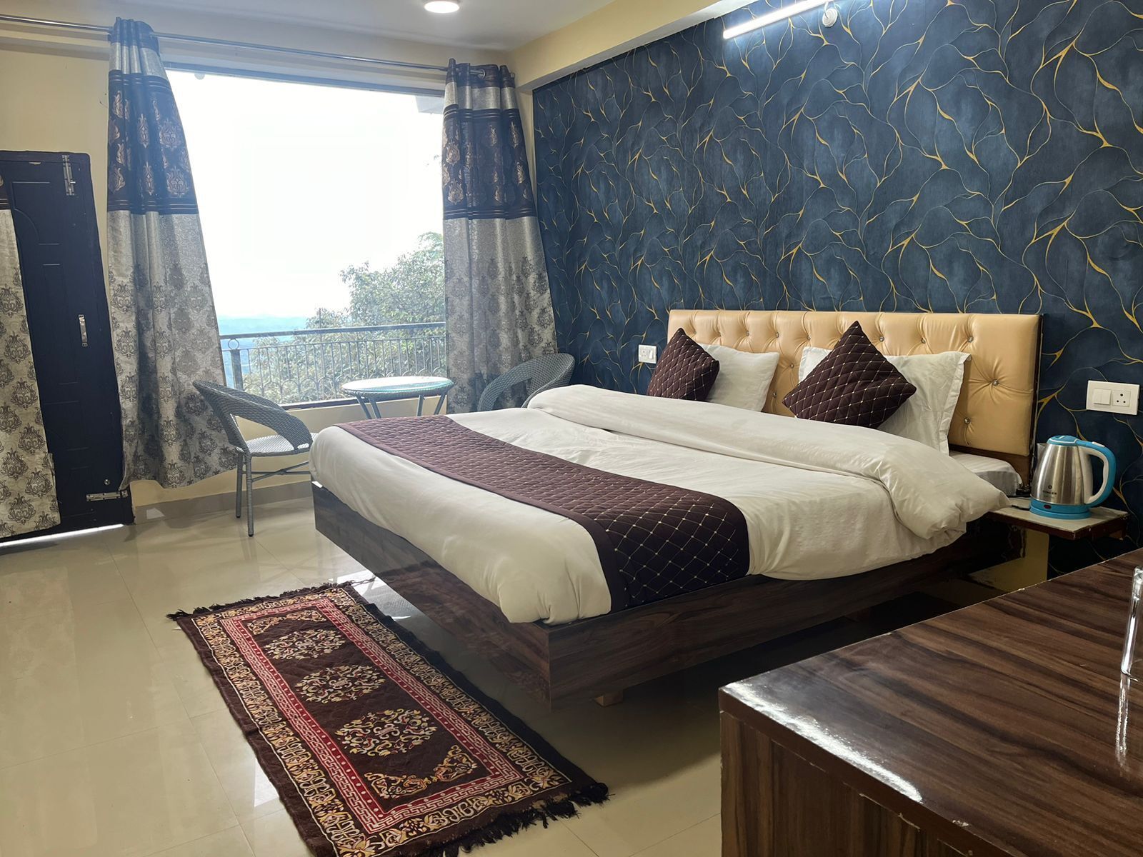 Habitación de hotel con cama, una mesita, una silla, cafetera y vista al exterior.