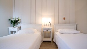 A hotel room with two single beds, a bedside table with a lamp, and a small bedside table with a plant and book. - Stunning 2-bed House in Lefkas (Lefkada)