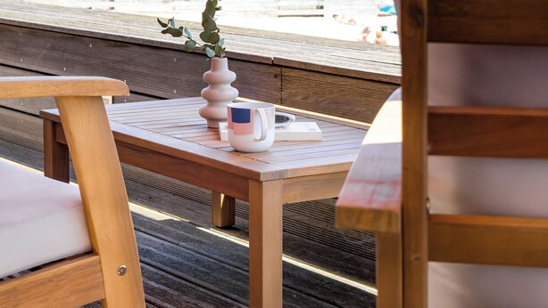 Um deck de madeira com mesa, cadeiras e vista para a praia e o oceano.