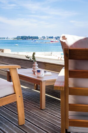 Eine Holzterrasse mit Tisch, Stühlen und Blick auf Strand und Meer.