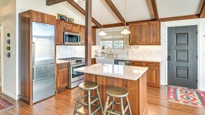A modern kitchen with wooden cabinets, stainless steel appliances, a central island with stools, and exposed wooden beams. - Cozy Mtn-View Chalet < 2 Mi to Windham Slopes (Windham)
