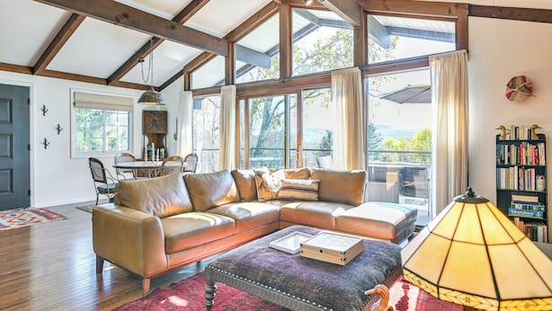 A spacious living room with a large sectional sofa, a coffee table, and a lamp. There is a bookshelf and a dining area visible in the background. - Cozy Mtn-View Chalet < 2 Mi to Windham Slopes (Windham)