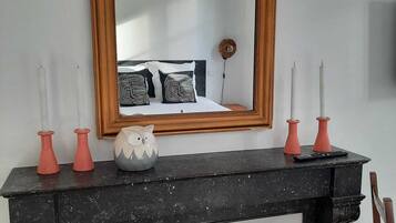 Une chambre avec un grand miroir au-dessus d’une cheminée, un lit agrémenté d’oreillers à motifs et des vases décoratifs posés sur le manteau de la cheminée.