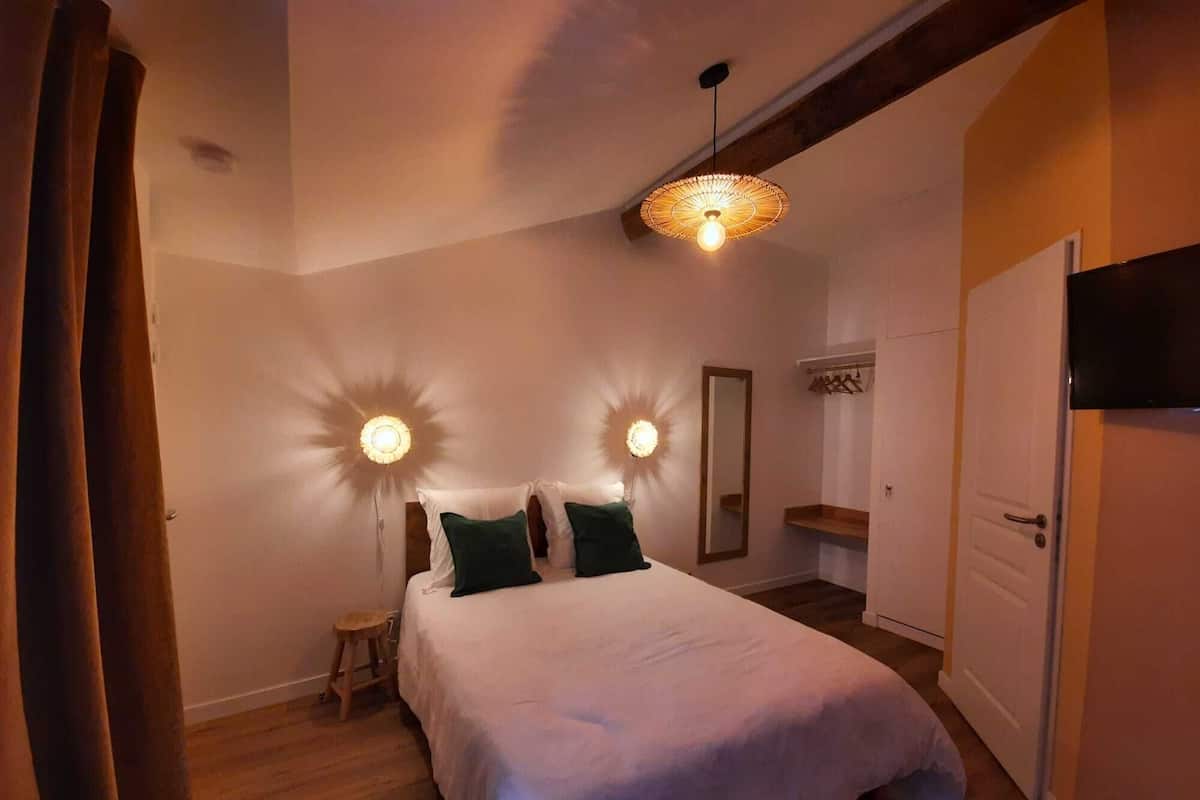 A bedroom with a bed, two wall sconces, a hanging light, a mirror, and a wardrobe.