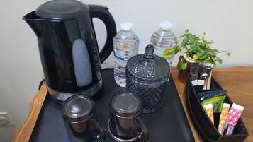 Una bandeja con una cafetera negra, dos tazas de vidrio, una botella de agua, una jarra de vidrio y una planta con un sujetavasos que contiene varios objetos.