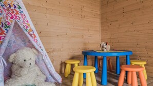 Ein Zimmer mit Holzboden, einem blauen Tisch mit gelben und orangen Hocker, einem weißen Teddybären und einem bunten Zelt.