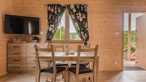 Ein Holzambiente mit Esstisch, Stühlen, einem Fernseher und einem Fenster mit blumigem Vorhang.