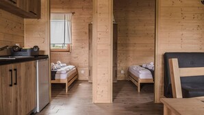 A compact wooden cabin with two single beds, a kitchenette, and a large window.