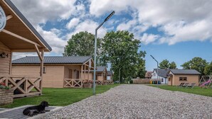A row of wooden cabins with a gravel path in front, a dog on the path, and a clear sky.