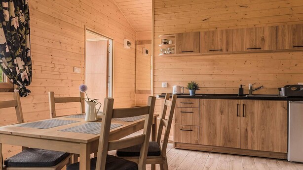 A wooden interior with a dining table, chairs, a kitchen area, and a door.